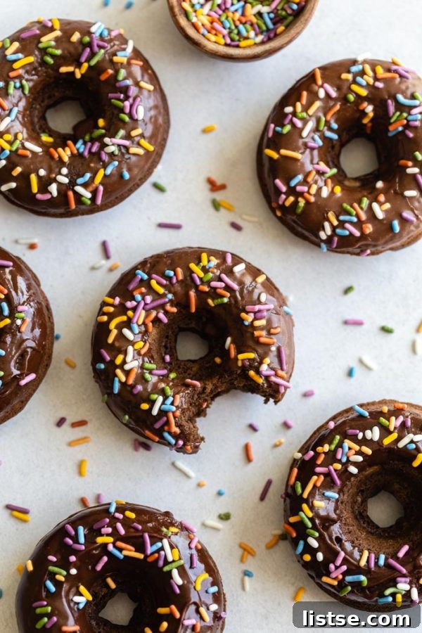 No-Fry Chocolate Donuts 4 chocolate glazed donuts topped with sprinkles and sprinkles all around the shot. The center donut in the shot has a bite taken out