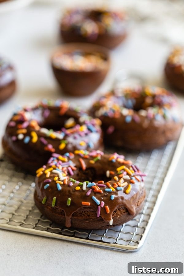 No-Fry Chocolate Donuts 5 chocolate glazed donuts topped with sprinkles and sprinkles all around the shot. the donuts are sitting on top of a cooling wrack