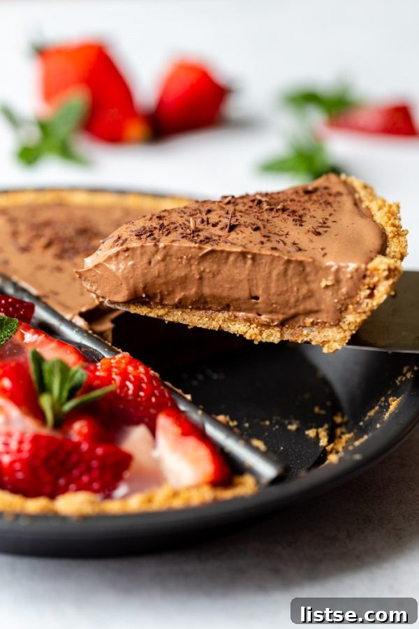 Sweet Divide Pie: Strawberry & Chocolate 5 Double-sided 'split decision pie' featuring a chocolate silken pie on one side and a fresh strawberry pie on the other. Fresh strawberries and mint are around the edges of the frame. This image shows an up-close shot of a piece of chocolate pie being lifted from the dish, highlighting its perfect texture.
