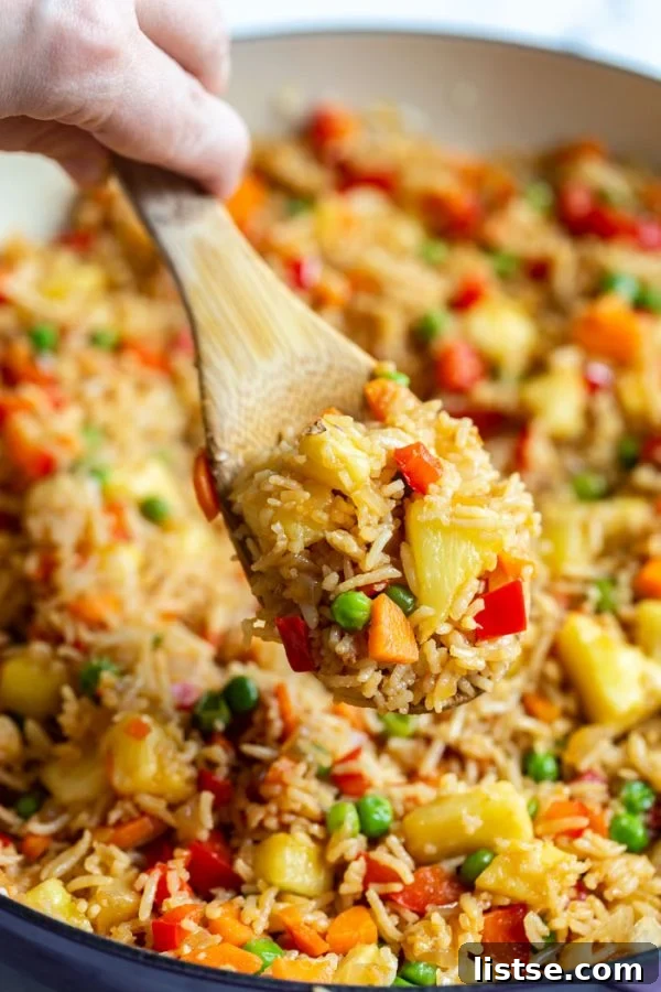 Golden Pineapple Fried Rice 3 shot of fried rice in a large skillet with peas, pineapple, red bell pepper, and carrot. a scoop of the rice is being taken out, highlighting the inviting texture and rich ingredients
