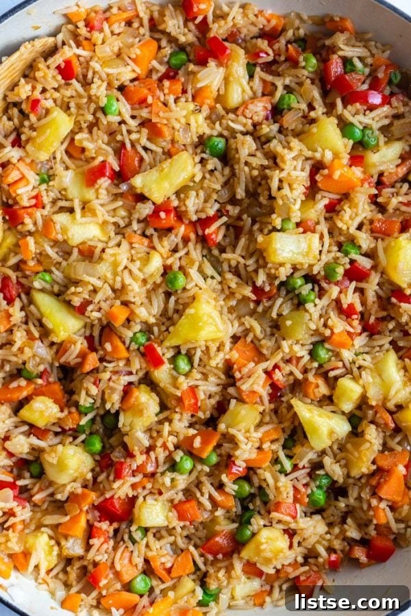 Golden Pineapple Fried Rice 4 top down shot of fried rice in a large skillet with peas, pineapple, red bell pepper, and carrot, highlighting the vibrant colors and appealing texture of the dish