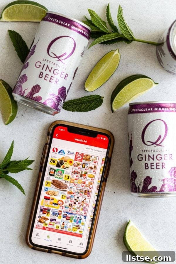Overhead shot of an iPhone displaying the Safeway app, surrounded by Q Ginger Beer cans, lime wedges, and fresh mint sprigs