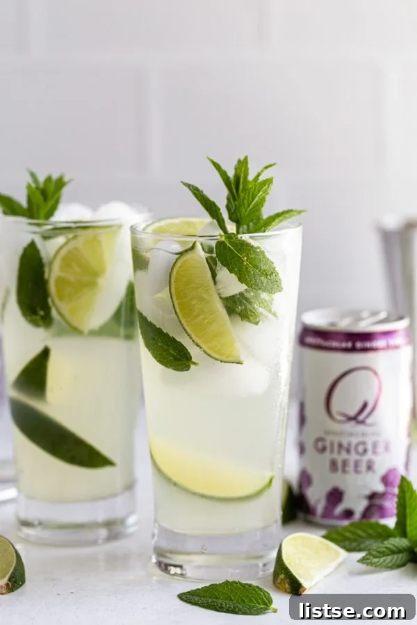 Another view of a Ginger Beer Mojito next to a Q Ginger Beer can, with vibrant lime wedges and fresh mint leaves