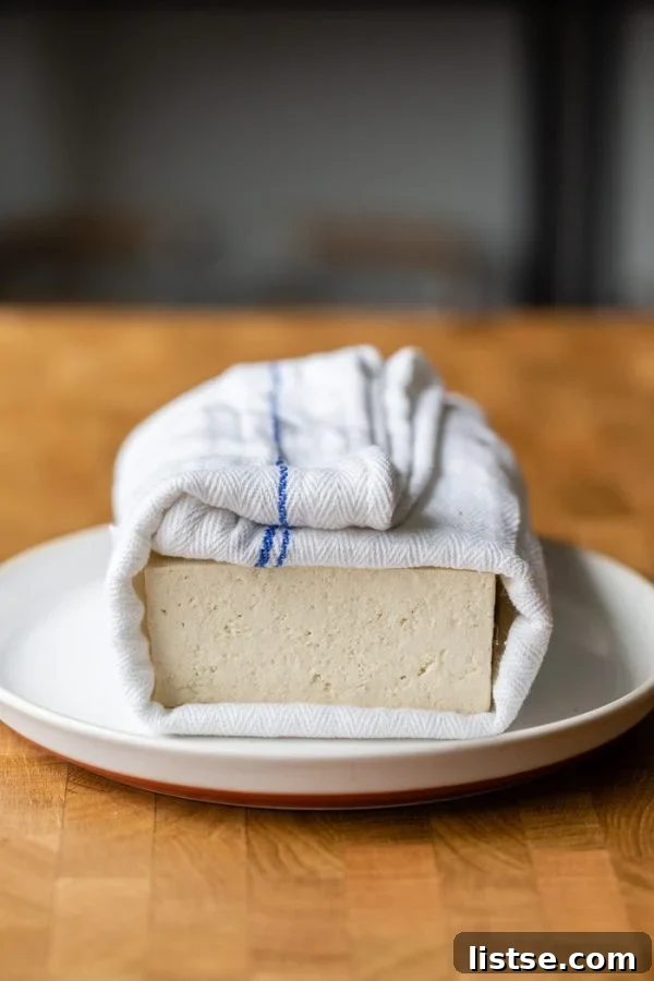 block of tofu wrapped in a white and blue towel, sitting on a white plate. It's all on a butcher block counter