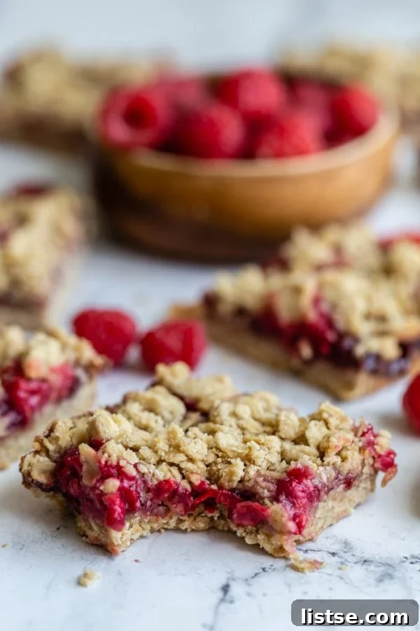 Close-up of a raspberry crumble bar showing the distinct layers of crust, jam, fresh raspberries, and crumb topping.
