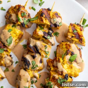 Grilled tofu satay skewers with peanut sauce on a white plate, ready to be served.