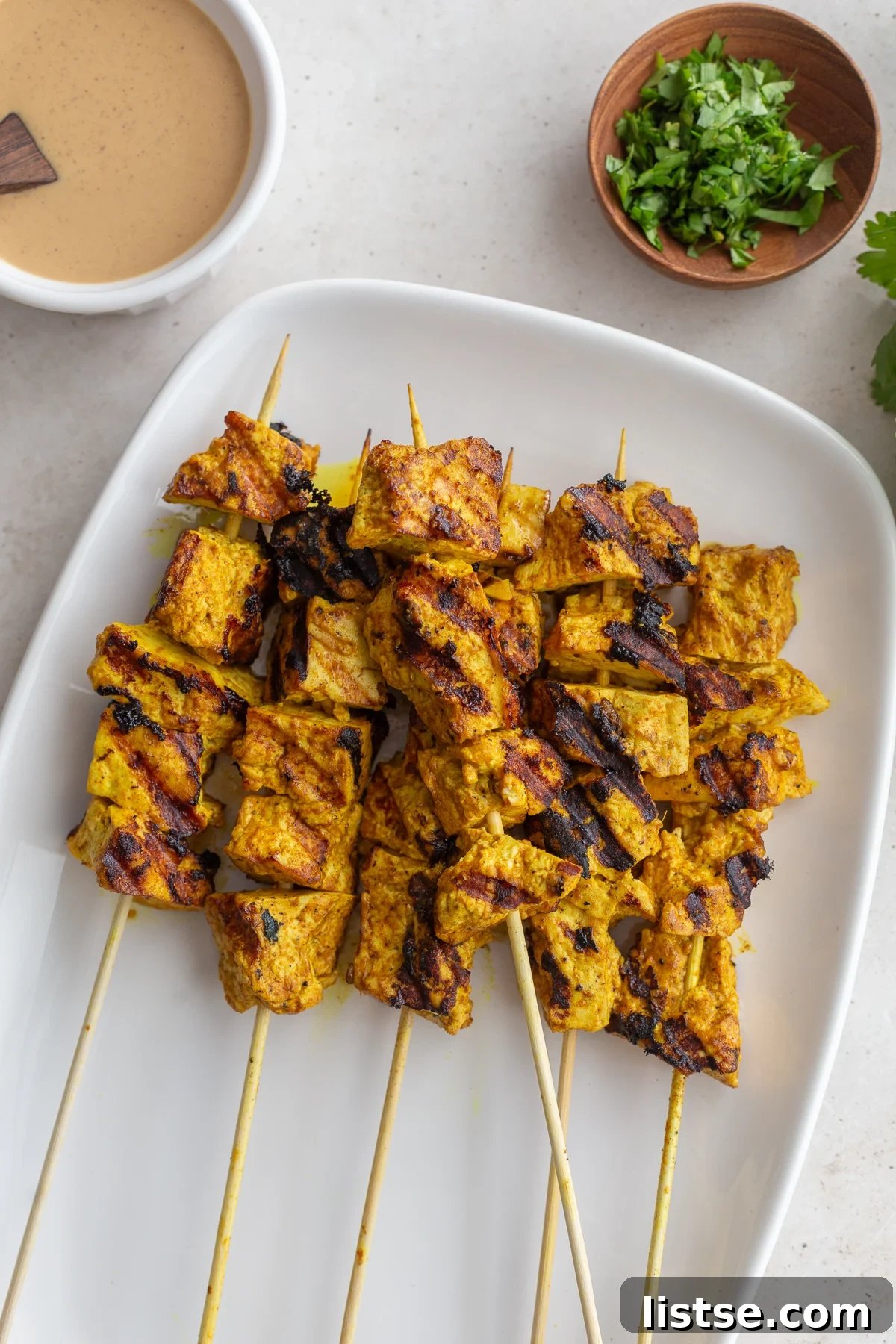Golden Tofu Satay with Velvety Peanut Sauce 9 Beautifully grilled tofu skewers with smoky char marks resting on a plate.