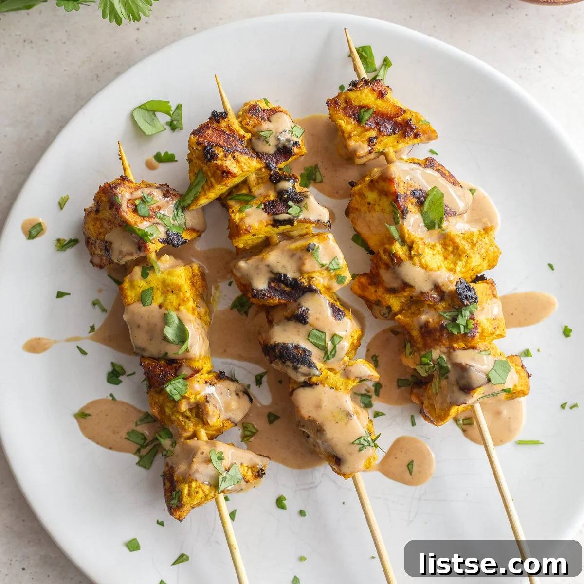 Golden Tofu Satay with Velvety Peanut Sauce 10 Grilled tofu satay drizzled with rich peanut sauce and garnished with fresh cilantro and a lime wedge on a white plate.