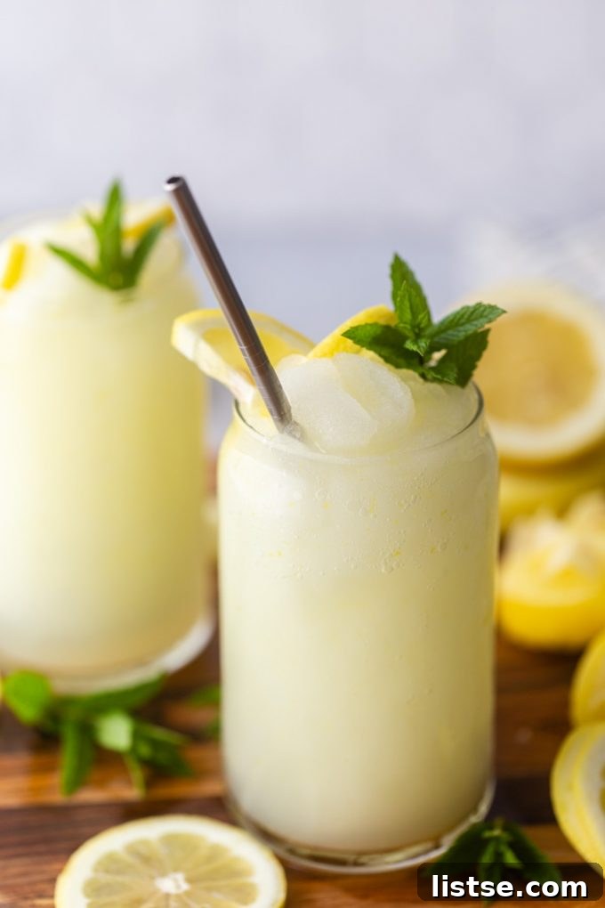 A vibrant glass of Boozy Frozen Lemonade, garnished with a fresh lemon slice, glistening with frost on a warm day.