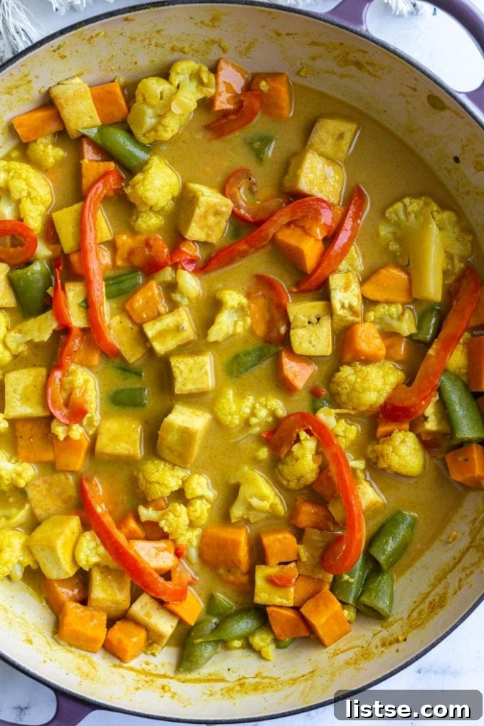 A top-down view of a skillet filled with golden-yellow tofu coconut curry, featuring red bell pepper, tender cauliflower florets, tofu cubes, vibrant snap peas, and fresh cilantro.