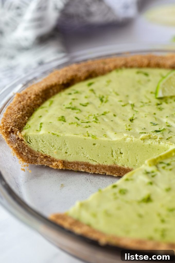 Close-up of a whole vegan key lime pie with one slice missing, highlighting its smooth, green filling.