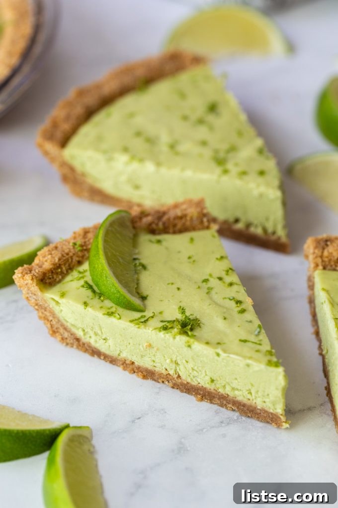 Several slices of green vegan key lime pie topped with lime zest and lime wedges, arranged on a marble board with whole limes.