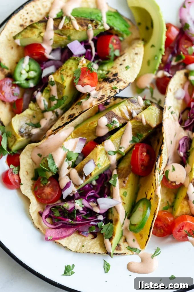 A vibrant platter of grilled avocado tacos, generously topped with slaw and spicy mayo.