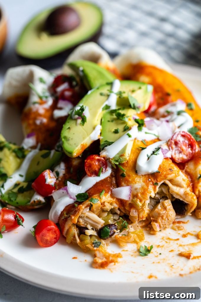 Pulled Jackfruit Enchiladas 3 An enticing close-up shot revealing the inside of a jackfruit enchilada, showcasing the tender shredded jackfruit filling. The dish is beautifully garnished with vibrant green avocado slices, diced red tomatoes, a swirl of vegan sour cream, and thinly sliced red onion.
