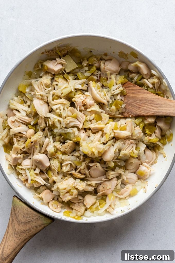Pulled Jackfruit Enchiladas 4 A white skillet filled with a savory mixture of shredded jackfruit, caramelized onions, and diced green chiles, creating the perfect base for the enchilada filling.