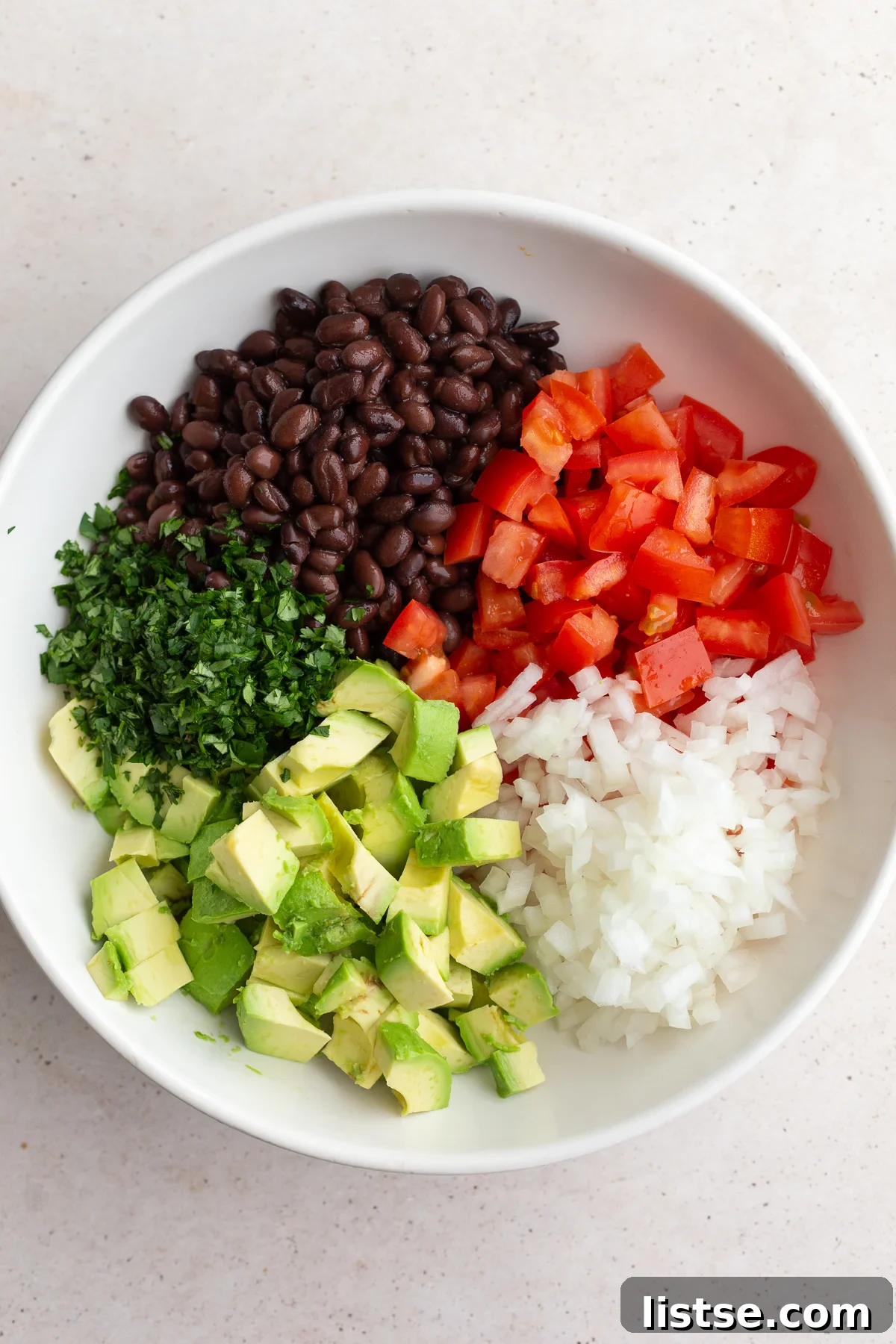 large bowl with diced avocados, tomatoes, onions, black beans, and cilantro, ready for dressing