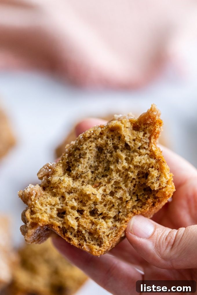 An inviting close-up shot of the interior of a sliced Coffee Cake Banana Muffin, revealing its moist, fluffy texture and pockets of banana goodness. A soft pink towel is visible in the background.