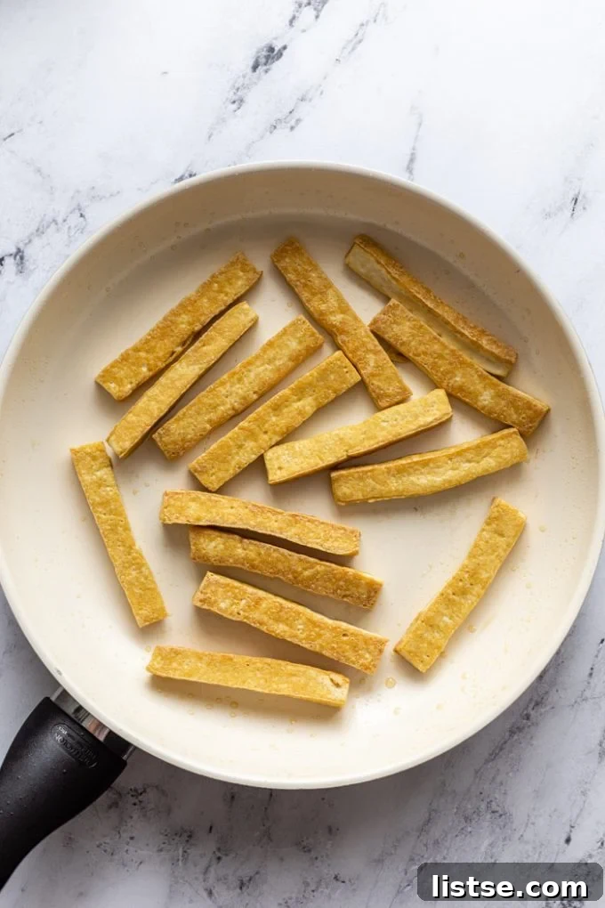 top down shot of a white skillet filled with strips of sauteed tofu