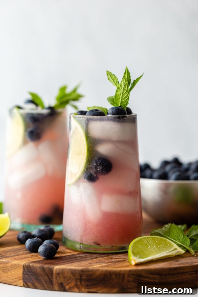 Another side profile of two Blueberry Mojitos, emphasizing the condensation on the glasses and the enticing presentation of the summer drink.
