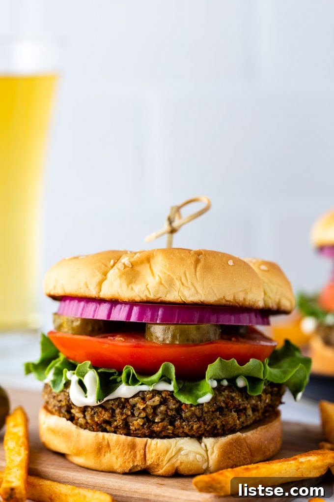 Irresistible Homemade Veggie Burgers 2 Straight-on shot of a perfectly cooked vegetarian burger on a toasted bun, generously topped with crisp lettuce, creamy mayo, fresh tomato slices, tangy pickles, and vibrant red onion. A refreshing beer and a side of golden French fries blur invitingly in the background.