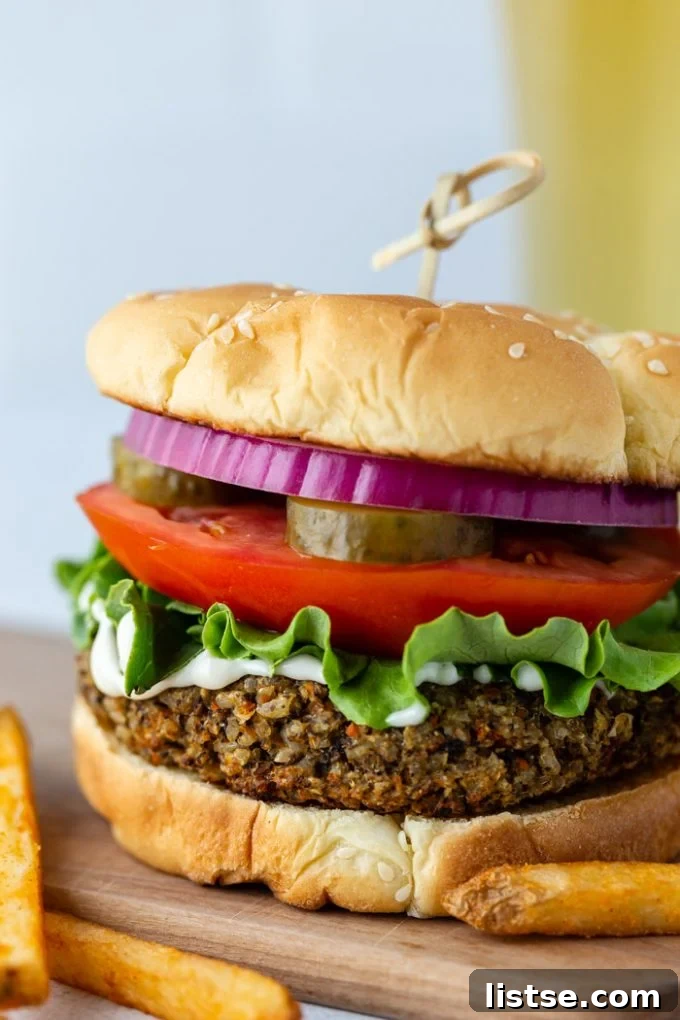 Irresistible Homemade Veggie Burgers 4 Another vibrant straight-on shot of a delicious vegetarian burger, served on a bun, piled high with fresh lettuce, creamy mayonnaise, ripe tomato, crunchy pickles, and thinly sliced red onion. A chilled beer and crispy French fries complete the classic burger meal in the background.