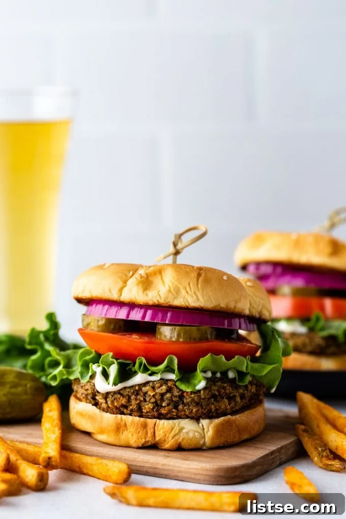 Irresistible Homemade Veggie Burgers 7 Another enticing straight-on view of a vegetarian burger, beautifully assembled on a bun and adorned with crisp lettuce, a generous dollop of vegan mayo, ripe tomato slices, crunchy pickles, and a vibrant ring of red onion. A refreshing beverage and golden French fries are visible in the soft background, completing the inviting meal.