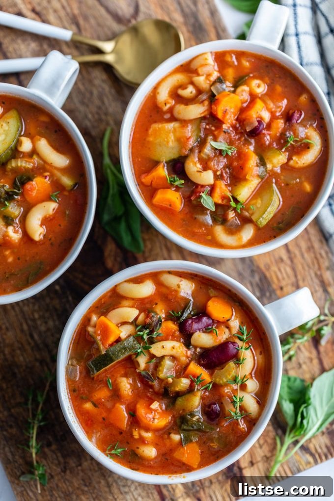 Hearty Vegan Minestrone 2 Several vegan minestrone soup portions served in stylish soup cups on a rustic wooden board, garnished with fresh herbs, ready to be enjoyed.