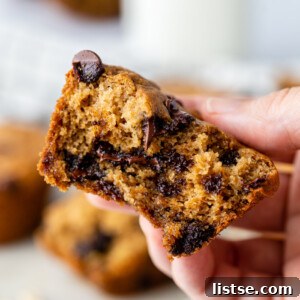 Close-up of a hand holding a half-eaten chocolate chip oat flour muffin.