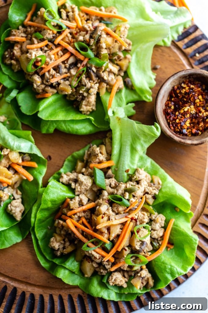 top down shot of vegan lettuce wraps filled with a tofu and mushroom mixture and topped with shredded carrots. all on a round wood board
