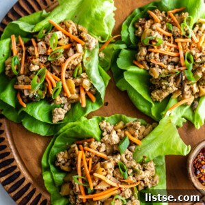 top down shot of vegan lettuce wraps filled with a tofu and mushroom mixture and topped with shredded carrots. all on a round wood board