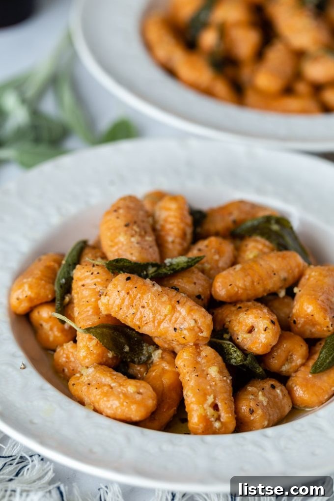 side shot of sweet potato gnocchi in a sage sauce. In a white bowl with another bowl in the background