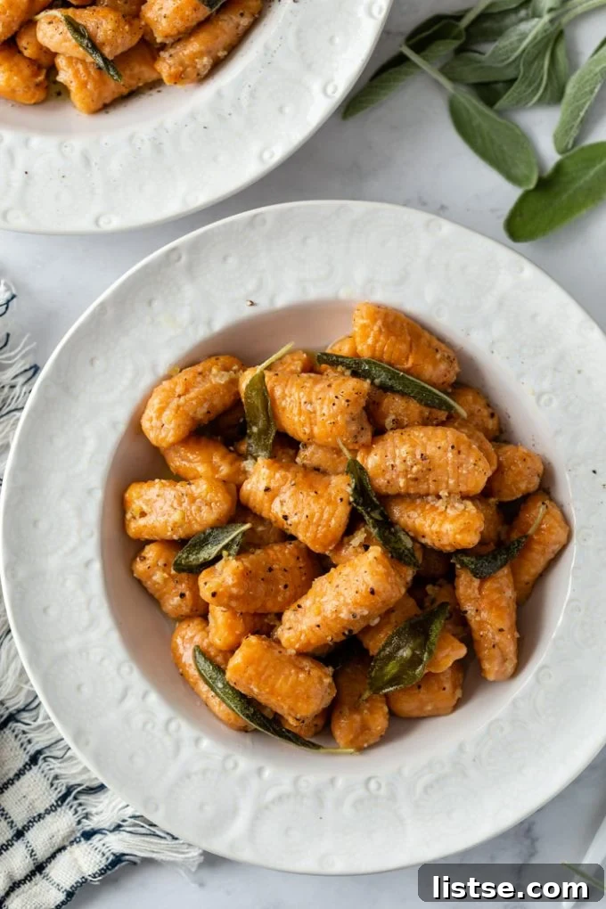 top down shot of sweet potato gnocchi in a sage sauce. In a white bowl with another bowl in the background