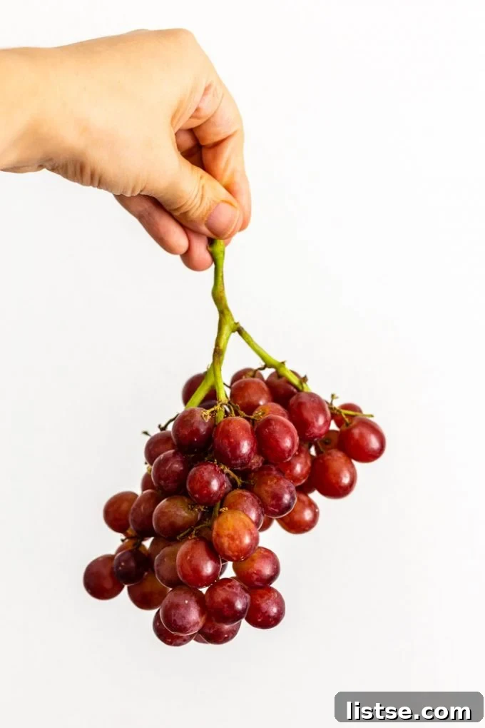 white female hand holding up a bunch of red grapes against a white background