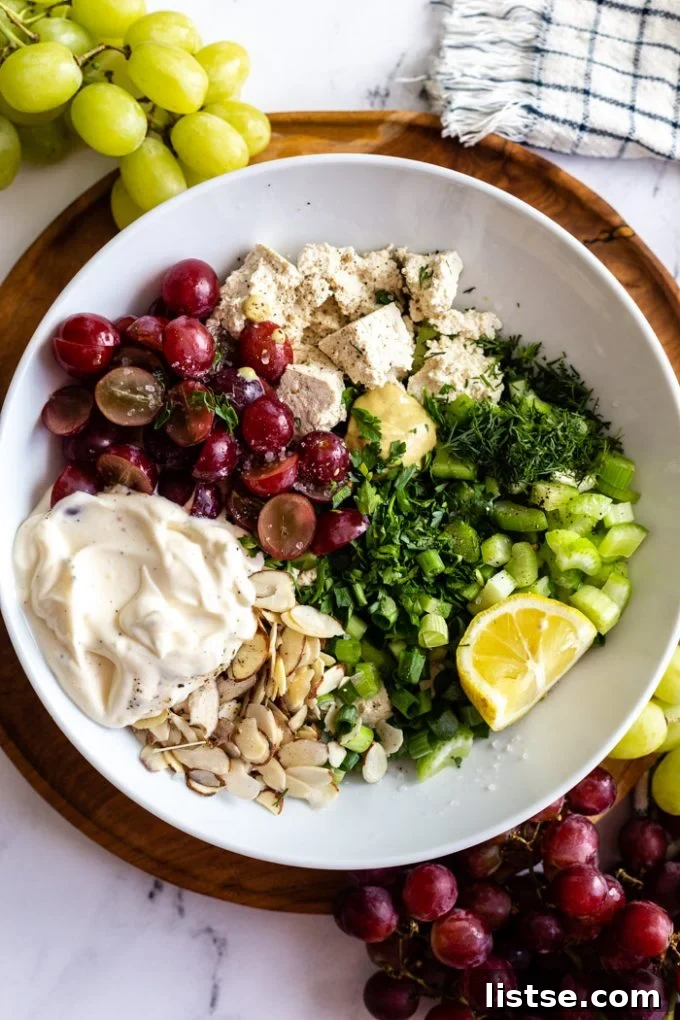 white bowl filled with the ingredients for this tofu chicken salad including red grapes, mayo, nuts, green onion, dill, tofu, lemon