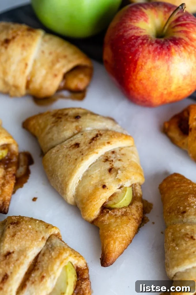 Flaky Apple Crescents 3 Platter of apple pie crescent rolls with fresh green apples and cinnamon sticks in the background, set on a rustic marble board.