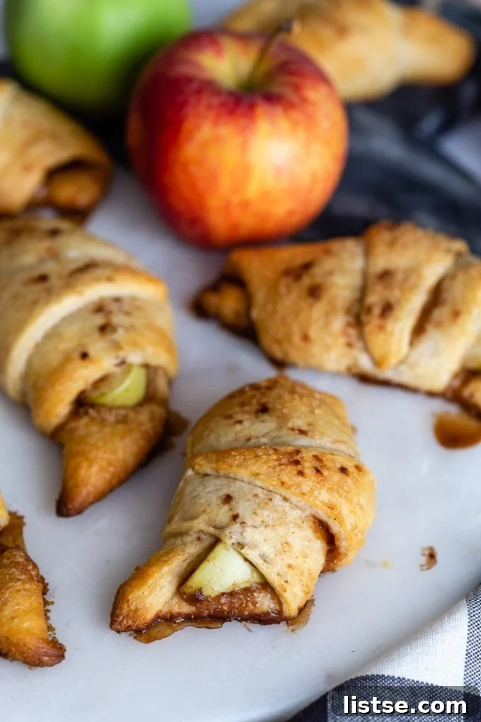 Flaky Apple Crescents 6 Close-up of golden, baked apple pie crescent rolls on a marble board, with blurred fresh apples in the background.