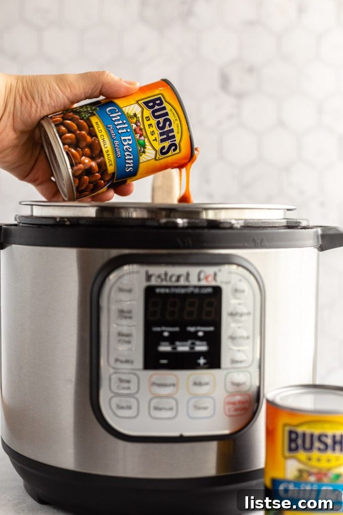 A can of BUSH'S Chili Pinto Beans being carefully poured into an Instant Pot, ready to become part of a delicious vegetarian chili.
