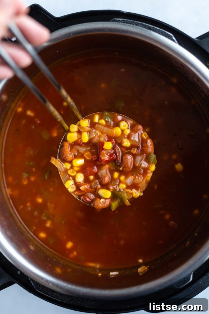 A large scoop of steaming vegetarian chili being lifted from an Instant Pot, showing its rich texture and vibrant ingredients.