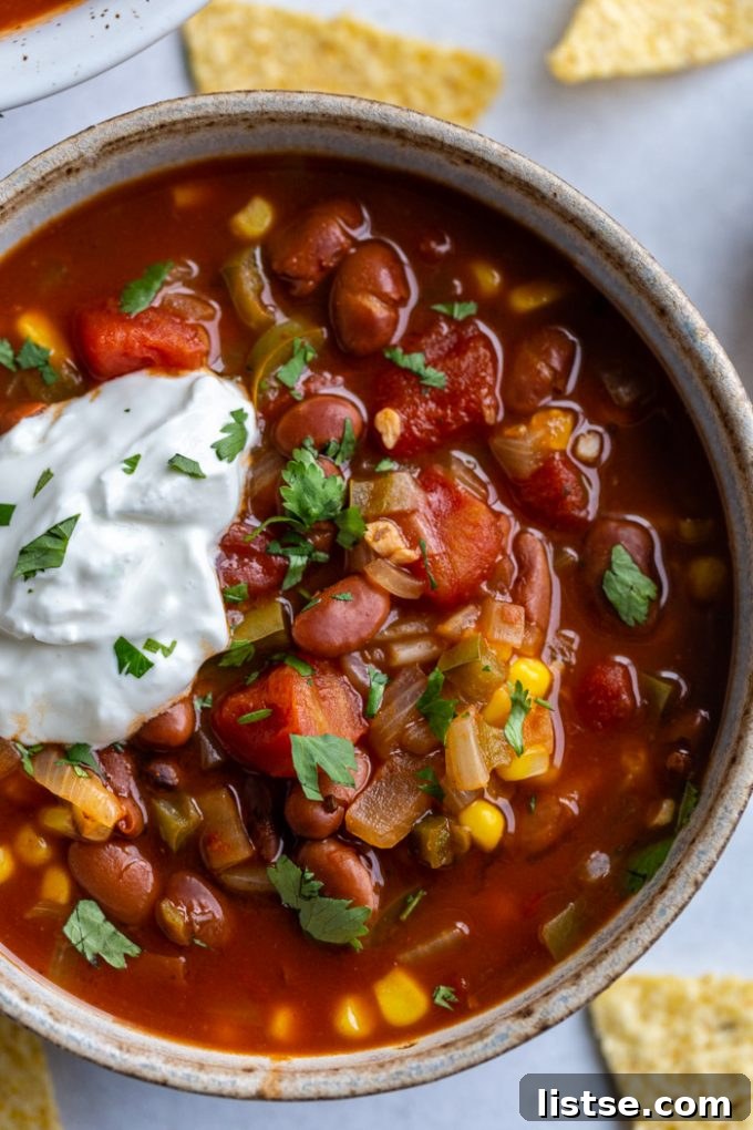 A beautifully presented bowl of vegetarian chili, generously topped with sour cream and fresh cilantro, with an emphasis on its rich texture and abundance of tomatoes and beans.
