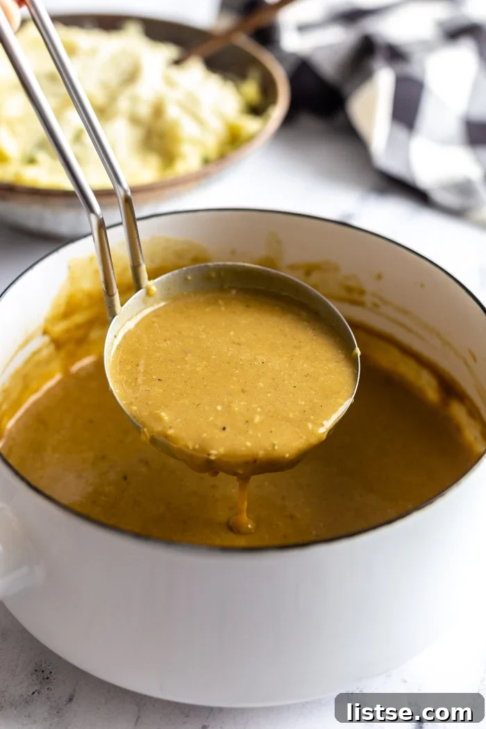 Effortless Vegan Gravy 4 white pot filled with brown vegan gravy and a laddle filled with gravy being pulled out of the pot