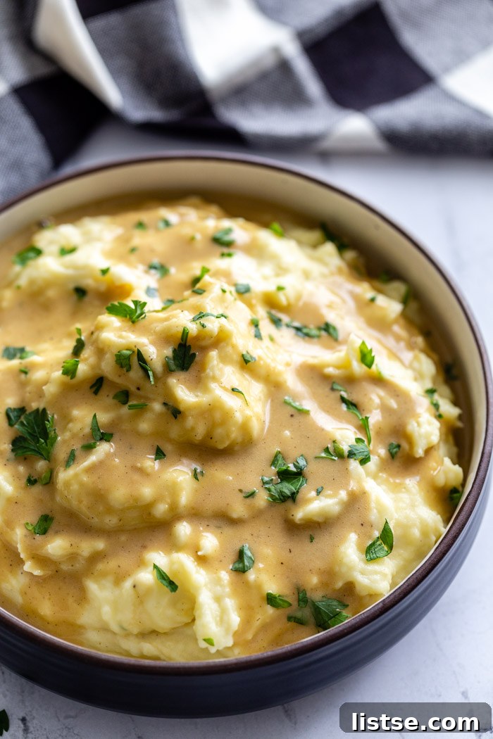 Effortless Vegan Gravy 10 big bowl of mashed potatoes covered with a brown vegan gravy sauce and sprinkled with fresh herbs