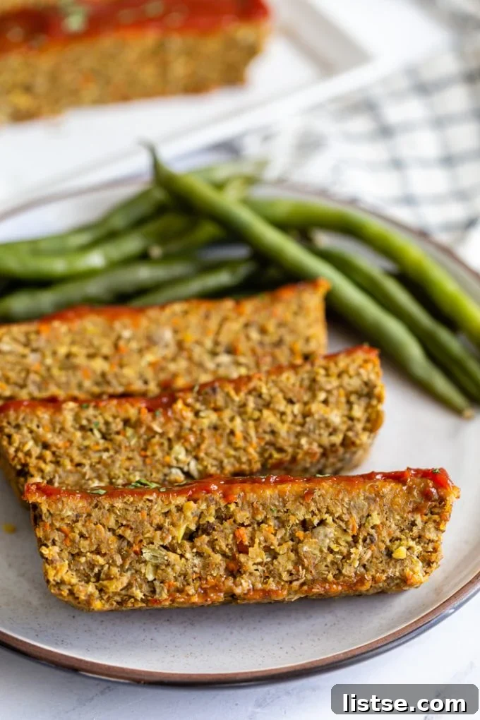 Hearty Plant-Based Loaf 3 Lentil meatloaf slice with a glossy ketchup topping and fresh parsley, accompanied by green beans on a white plate