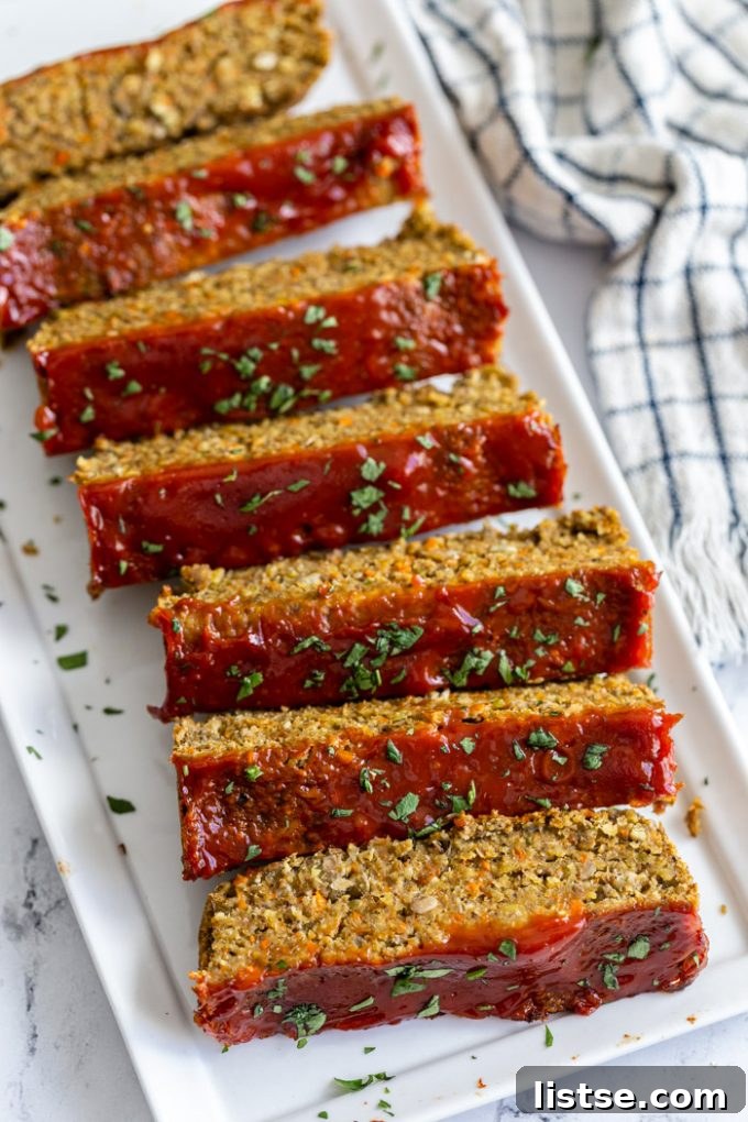 Hearty Plant-Based Loaf 5 Individual slices of vegan lentil meatloaf, perfectly browned and topped with a glossy ketchup glaze and fresh parsley, on a clean white plate
