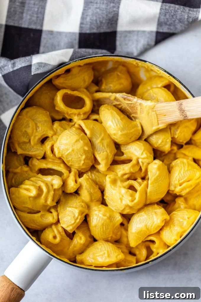 Top-down shot of a white pan filled with perfectly cooked macaroni noodles generously coated in a rich vegan cheese sauce, featuring a charming checkered towel in the corner.