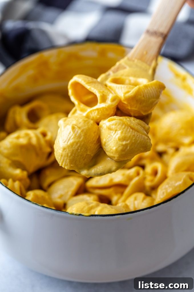 A pristine white pot filled with a generous serving of vegan pumpkin mac and cheese, with a soft towel draped in the background, inviting a cozy and comforting meal.