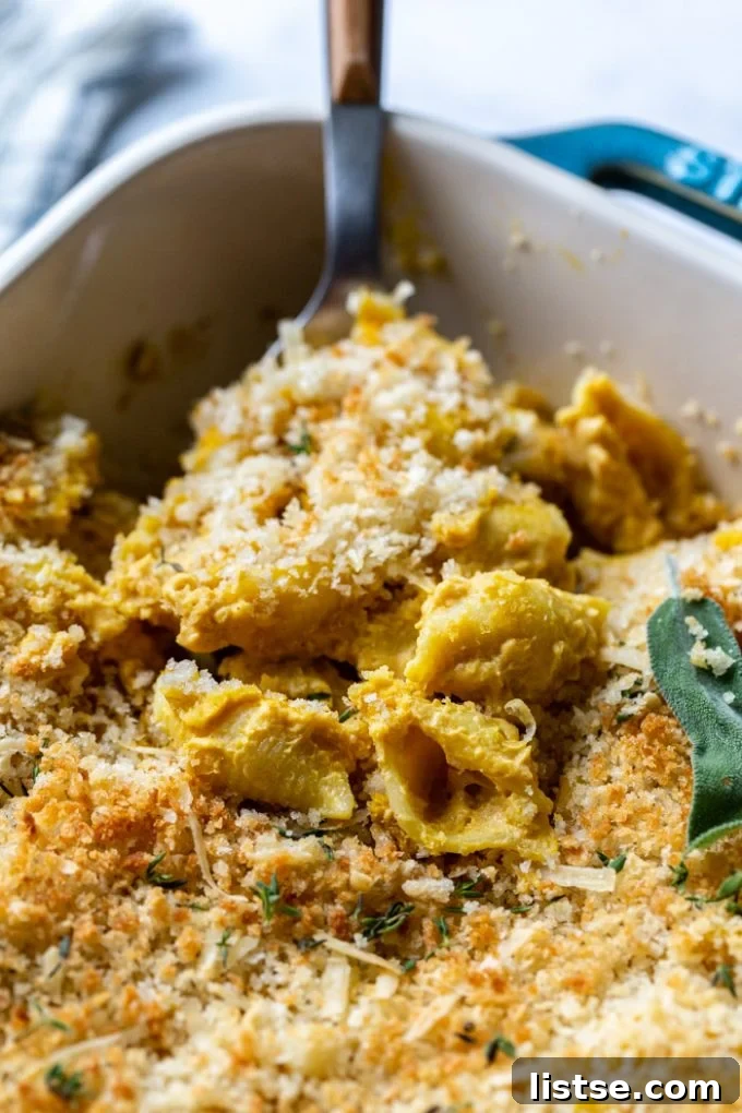 Scoop of baked vegan mac and cheese being pulled out of a casserole dish, showing the creamy texture and inviting appeal