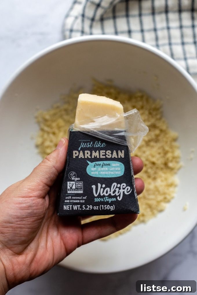 A block of Violife vegan parmesan cheese being held over a bowl of panko breadcrumbs, ready to be grated for the topping