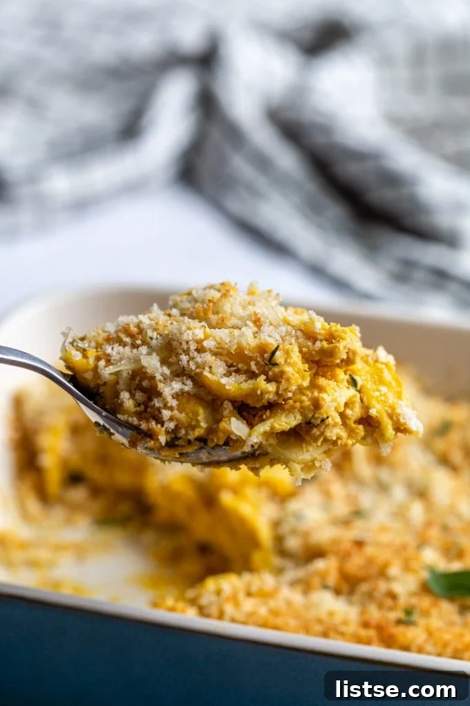 Scoop of mac and cheese being pulled out of a casserole dish, highlighting the contrast between the creamy pasta and crispy breadcrumbs