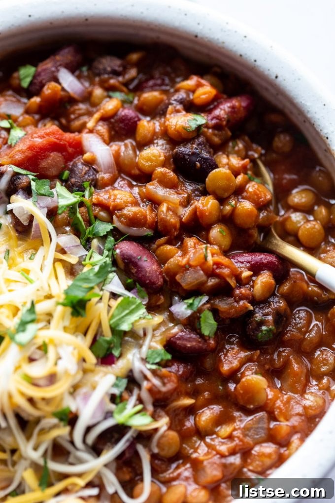 Hearty vegetarian chili, rich with lentils, served in a bowl with a spoon.