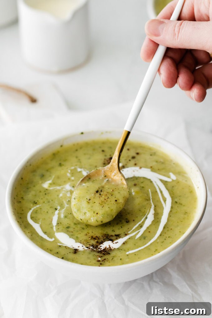 A spoon scooping up creamy vegan zucchini soup from a bowl, highlighting its smooth texture.